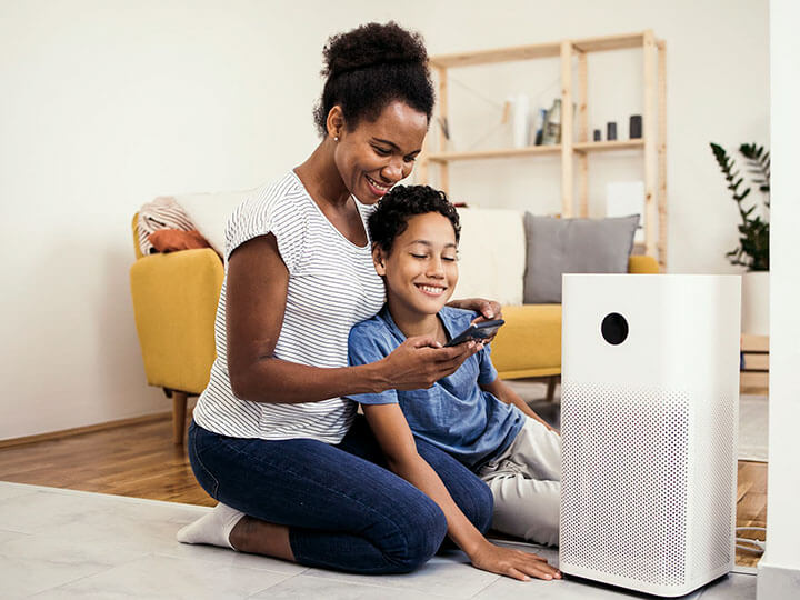 African American mother and son kneeling down next to air purifier controlling it with a phone